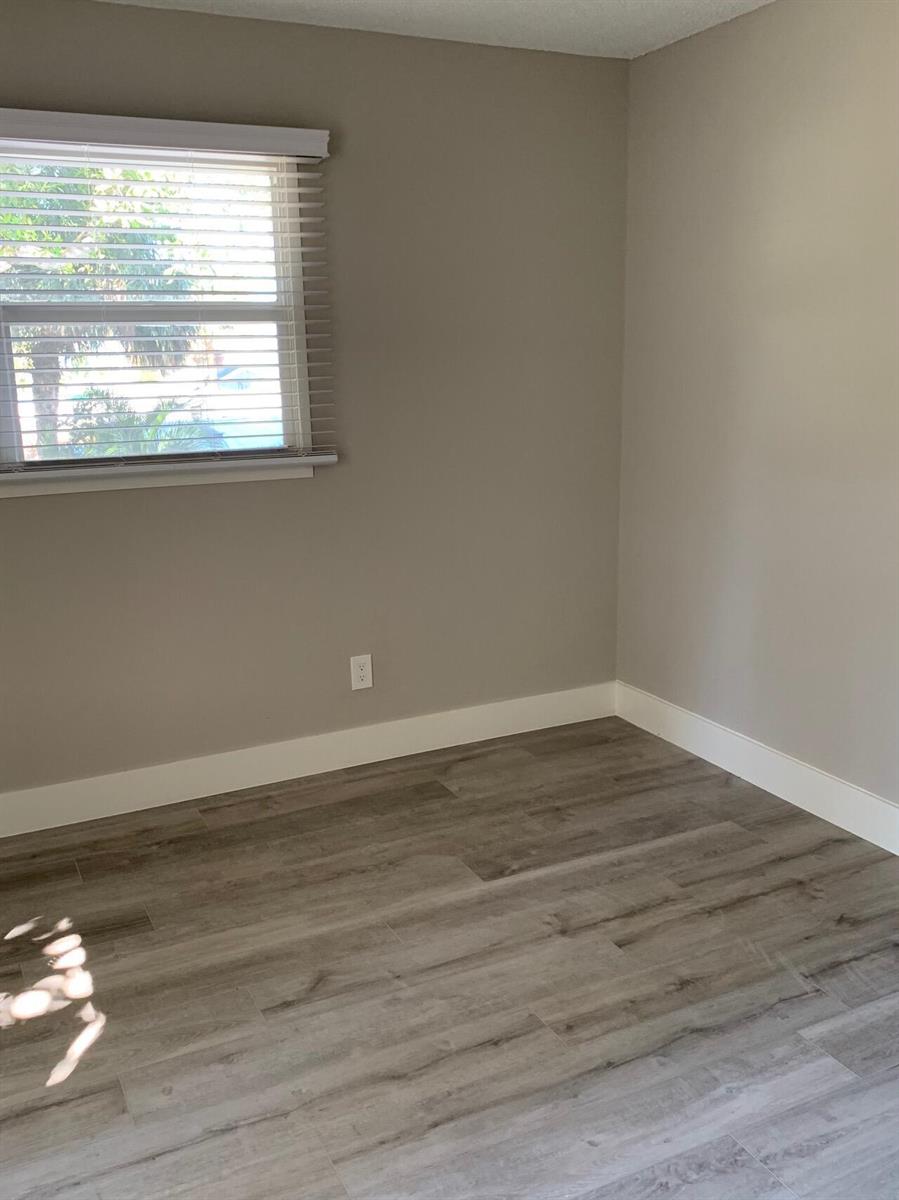 A bedroom with light gray walls, white baseboards, wood-look flooring, and a window with blinds — 4220 NE Indian River Drive NE Unit 5, Jensen Beach FL 34957, JENSEN BEACH, FL