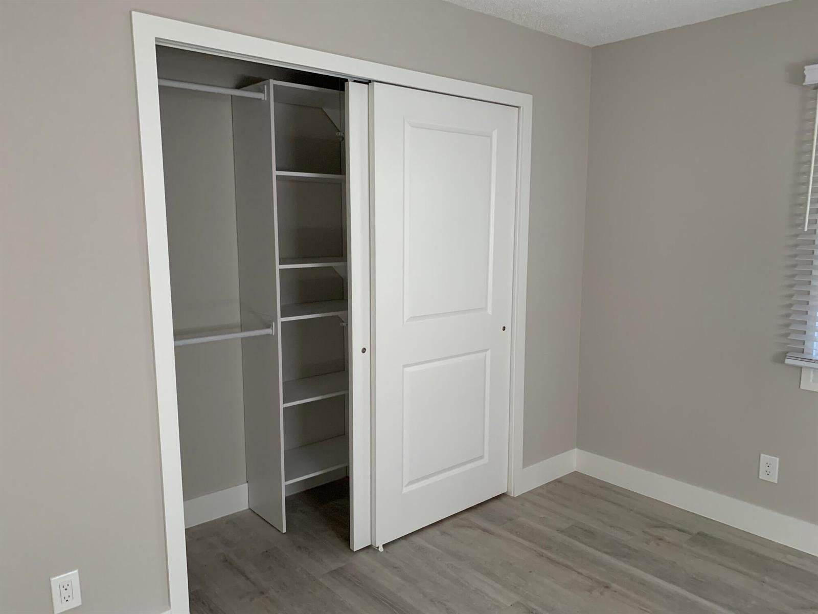 A bedroom features light wood-look flooring, gray walls, and a closet with white shelving — 4220 NE Indian River Drive NE Unit 5, Jensen Beach FL 34957, JENSEN BEACH, FL