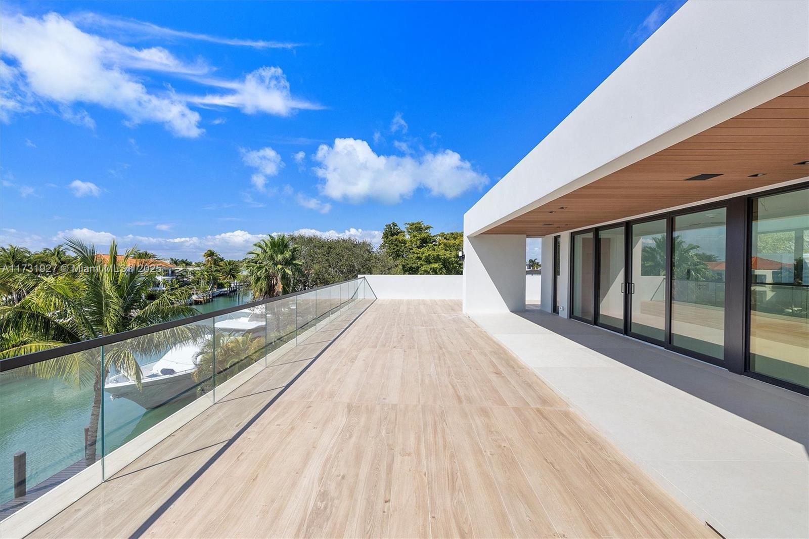 A modern balcony features wood-look tile flooring, a glass railing, and views of a canal — 960 Mariner Dr, Key Biscayne FL 33149, KEY BISCAYNE, FL