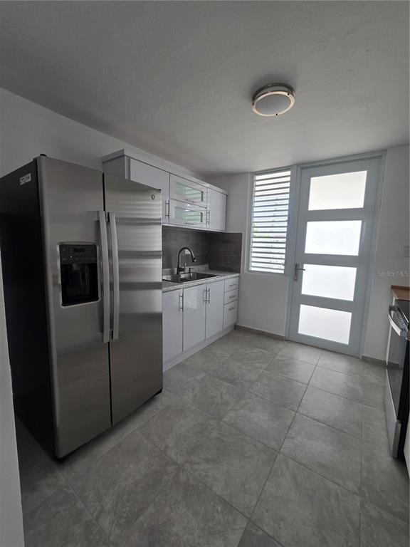 A kitchen features white cabinets, stainless steel appliances, gray tile flooring, and a glass-paneled door — . HIGUERO UNIT P7, CAROLINA, PR