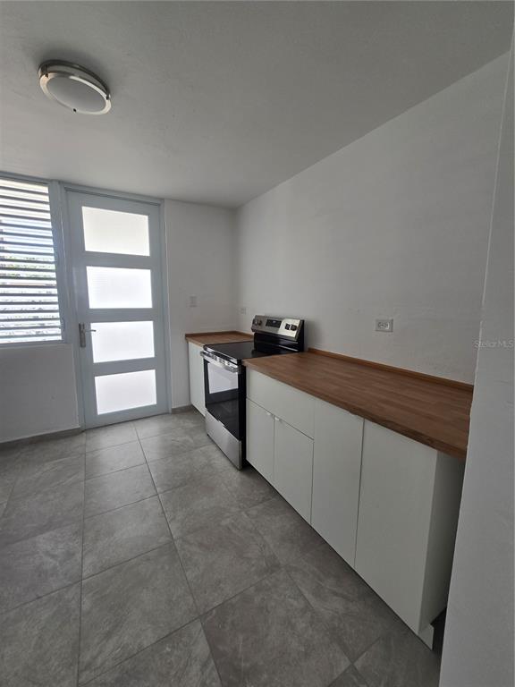 A kitchen features white cabinets, a wood countertop, a stainless steel stove, and tiled flooring — . HIGUERO UNIT P7, CAROLINA, PR