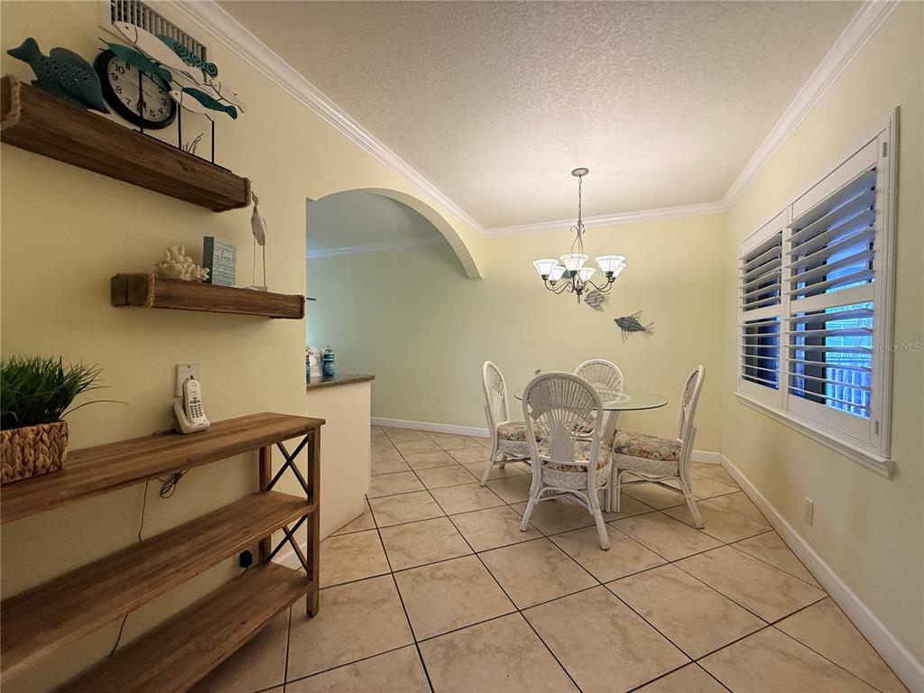A dining area features a glass-top table, wicker chairs, tile flooring, and coastal wall decor — 19417 GULF BOULEVARD UNIT D201, INDIAN ROCKS BEACH, FL