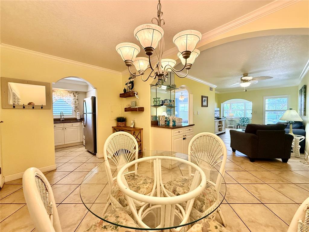 A dining area with a glass table and chandelier opens into a kitchen and living room — 19417 GULF BOULEVARD UNIT D201, INDIAN ROCKS BEACH, FL