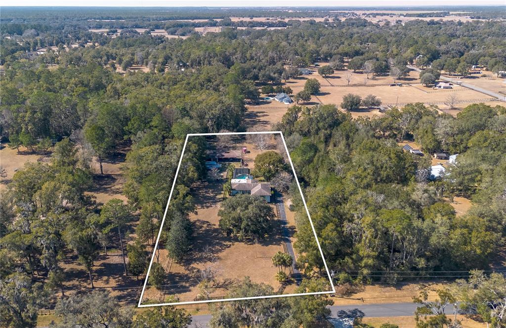 An aerial view shows a house with a pool on a large, wooded lot — 26 WOOD RIDGE DRIVE, OCALA, FL