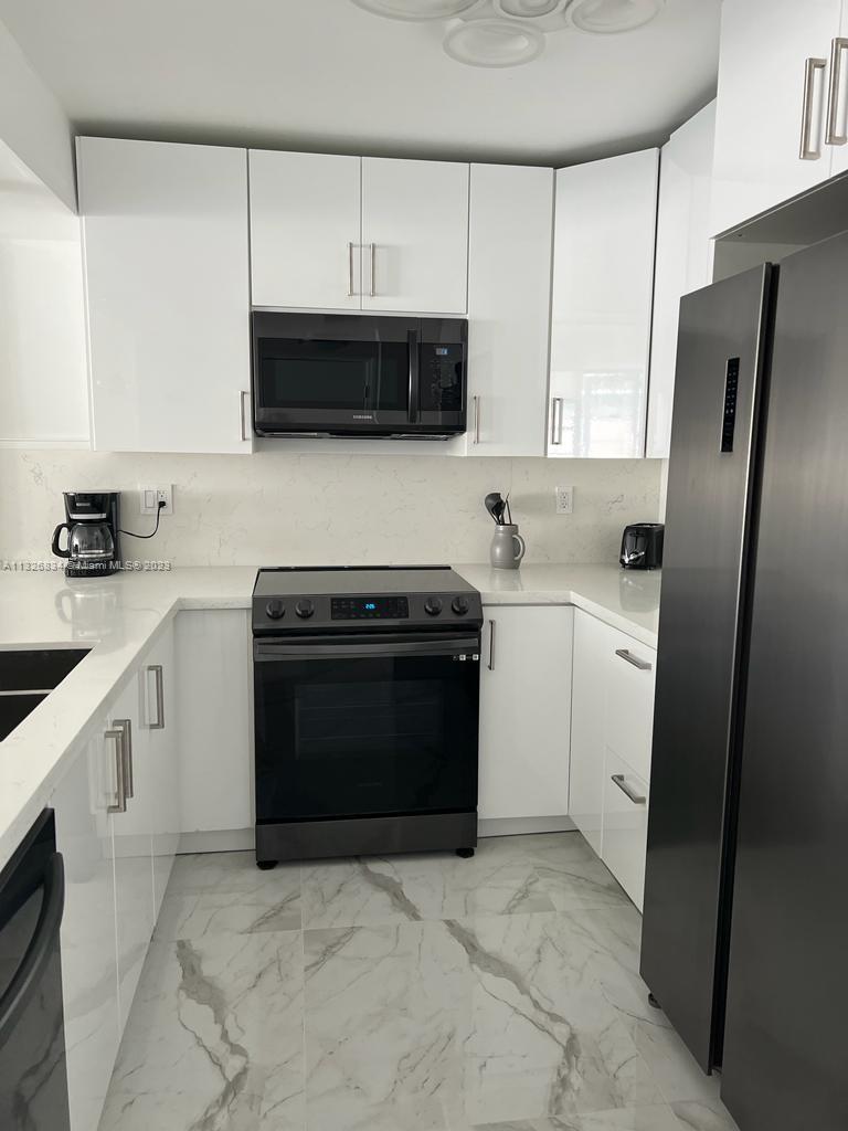 A modern kitchen features white cabinets, stainless steel appliances, and marble-patterned tile flooring — 3725 S Ocean Dr # 1503, Hollywood FL 33019, HOLLYWOOD, FL