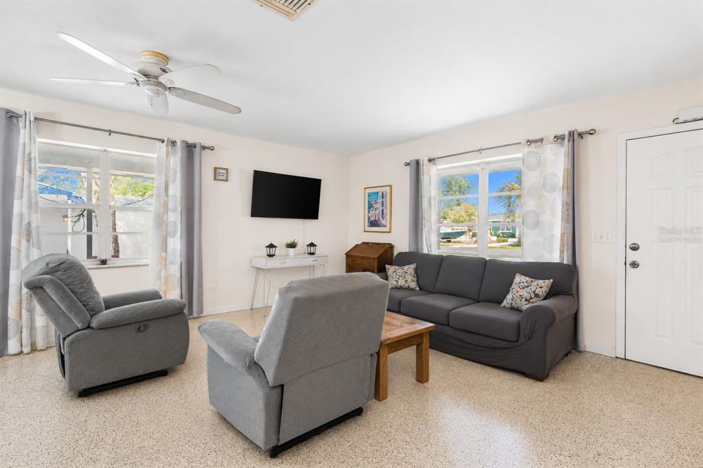 A living room features a grey sofa, two recliners, a television, and terrazzo flooring — 6816 TREEHAVEN DRIVE, SPRING HILL, FL