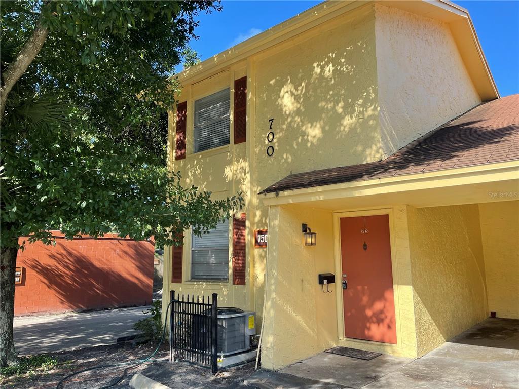 A two-story yellow stucco building features a covered entryway and a red front door — 7502 BOLANOS COURT, TAMPA, FL