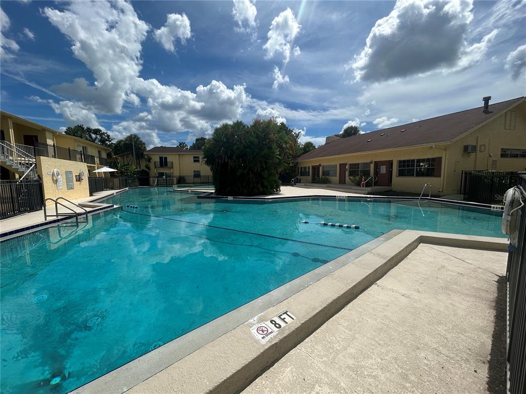 A large outdoor swimming pool surrounded by yellow apartment buildings under a cloudy blue sky — 7502 BOLANOS COURT, TAMPA, FL