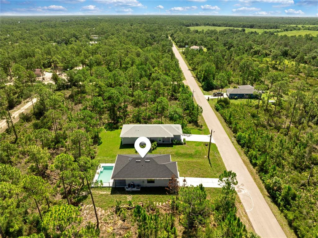 An aerial view shows two houses with pools surrounded by dense forest along a road — 27412 LAS LOMAS DRIVE, PUNTA GORDA, FL