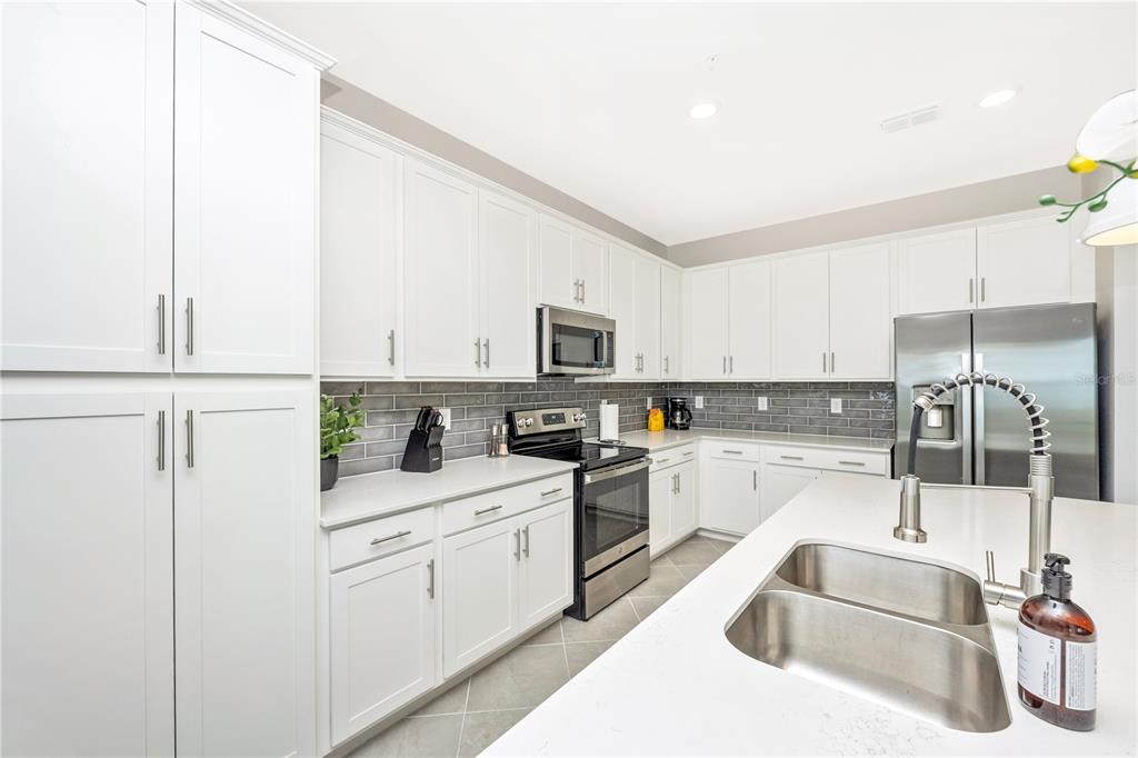 A modern kitchen features white cabinetry, stainless steel appliances, gray tile backsplash, and a quartz island — 12140 WELLEN GOLF STREET UNIT 401, VENICE, FL