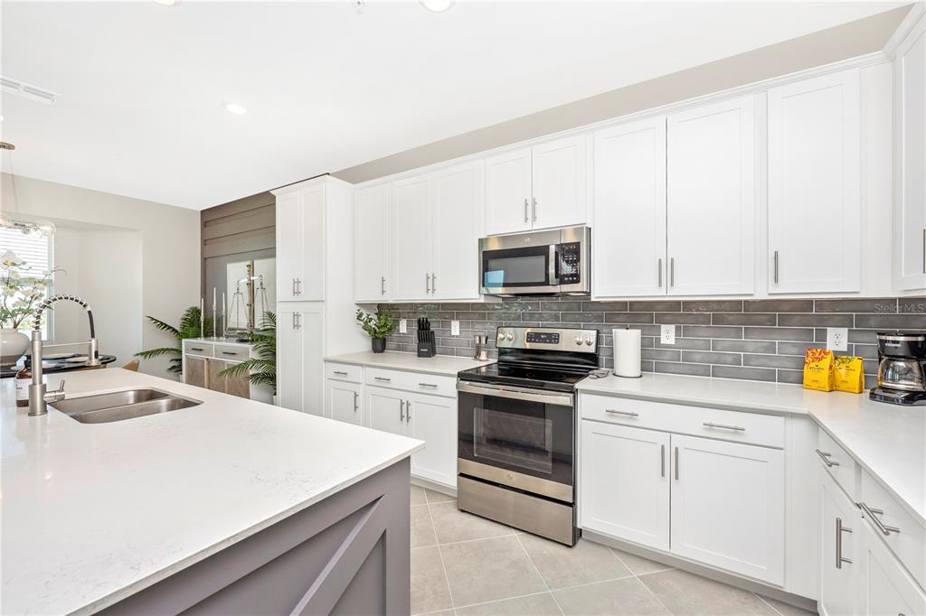 A kitchen features white cabinets, stainless steel appliances, a gray island, and a tiled backsplash — 12140 WELLEN GOLF STREET UNIT 401, VENICE, FL
