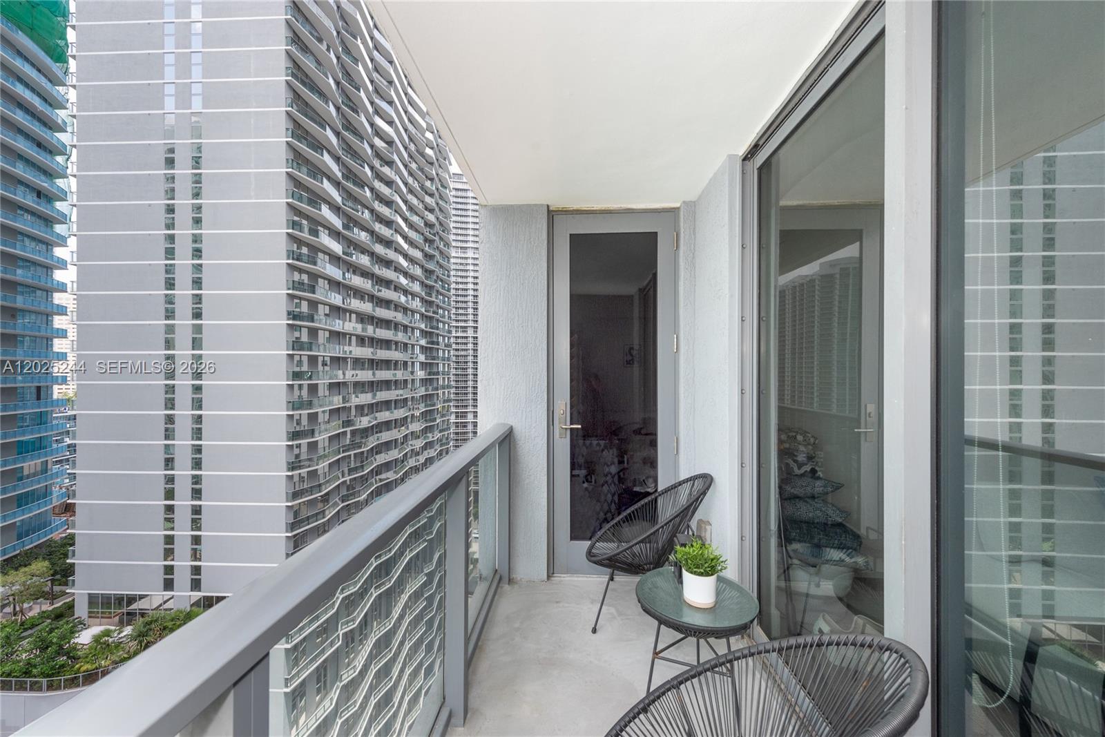 A balcony with two chairs, a small table, and a view of tall apartment buildings — 31 SE 6th St # 2506, Miami FL 33131, MIAMI, FL