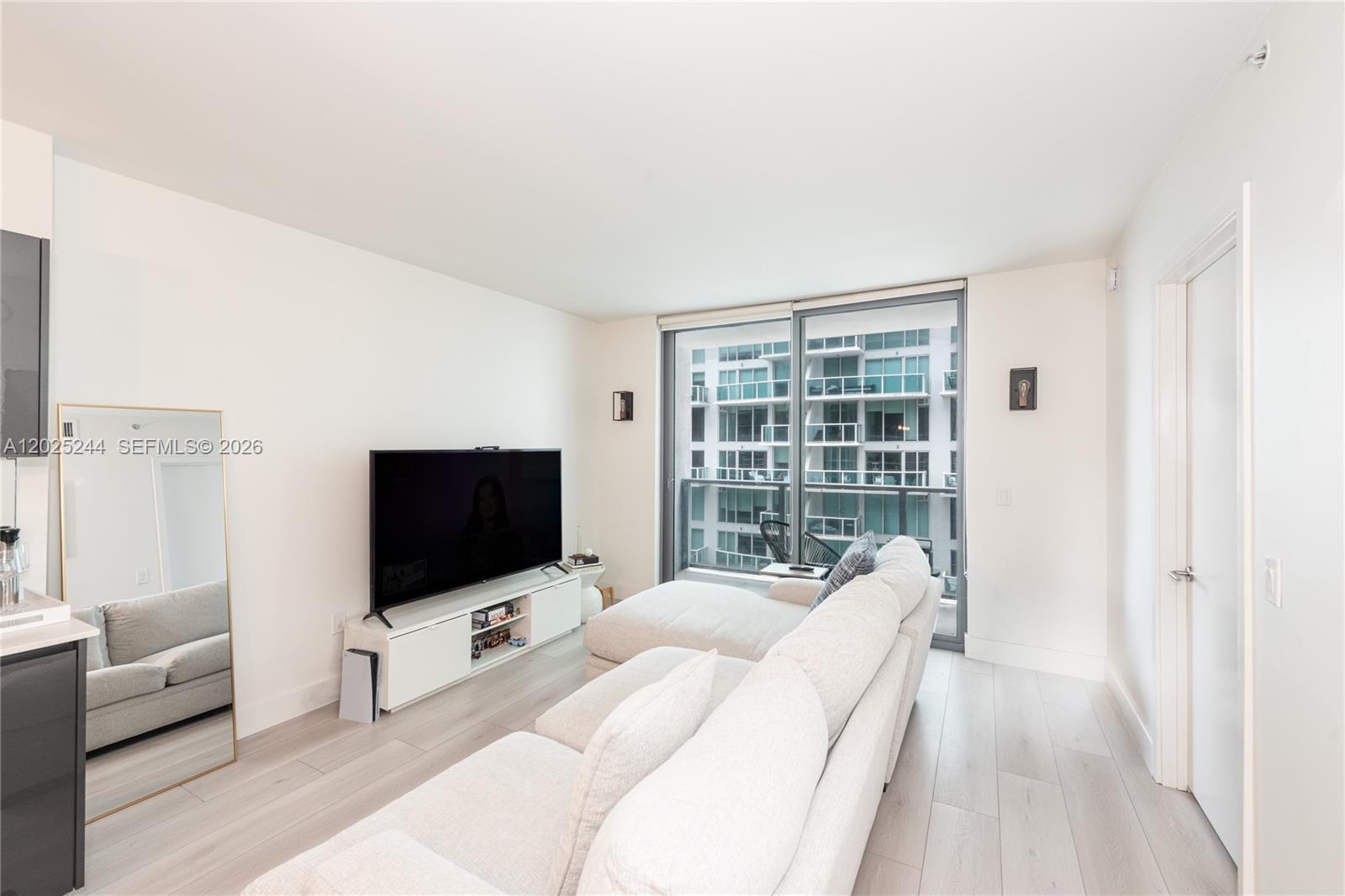 A living room features a white sectional sofa, a television on a console, and a balcony — 31 SE 6th St # 2506, Miami FL 33131, MIAMI, FL