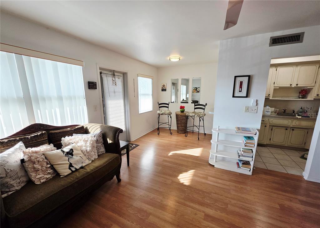 A living room with wood-look flooring, a sofa, a small dining area, and an adjacent kitchen — 5945 21ST STREET N UNIT 18, ST PETERSBURG, FL