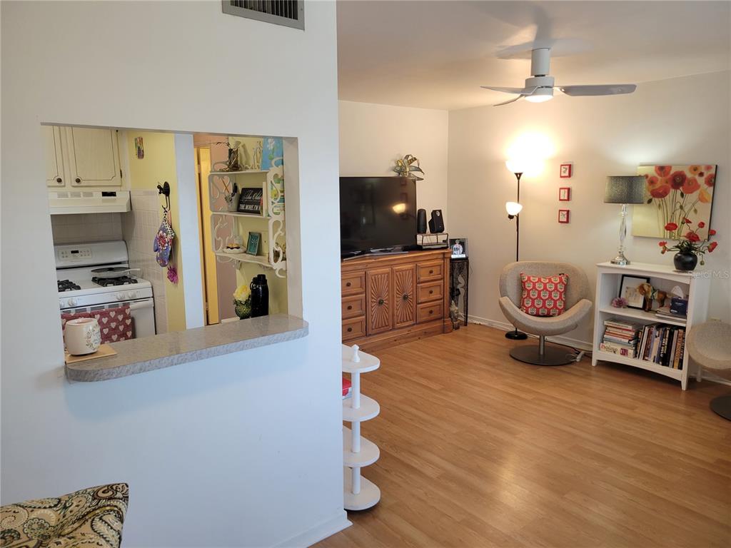 A living room with wood-look flooring, a ceiling fan, and a pass-through window to the kitchen — 5945 21ST STREET N UNIT 18, ST PETERSBURG, FL