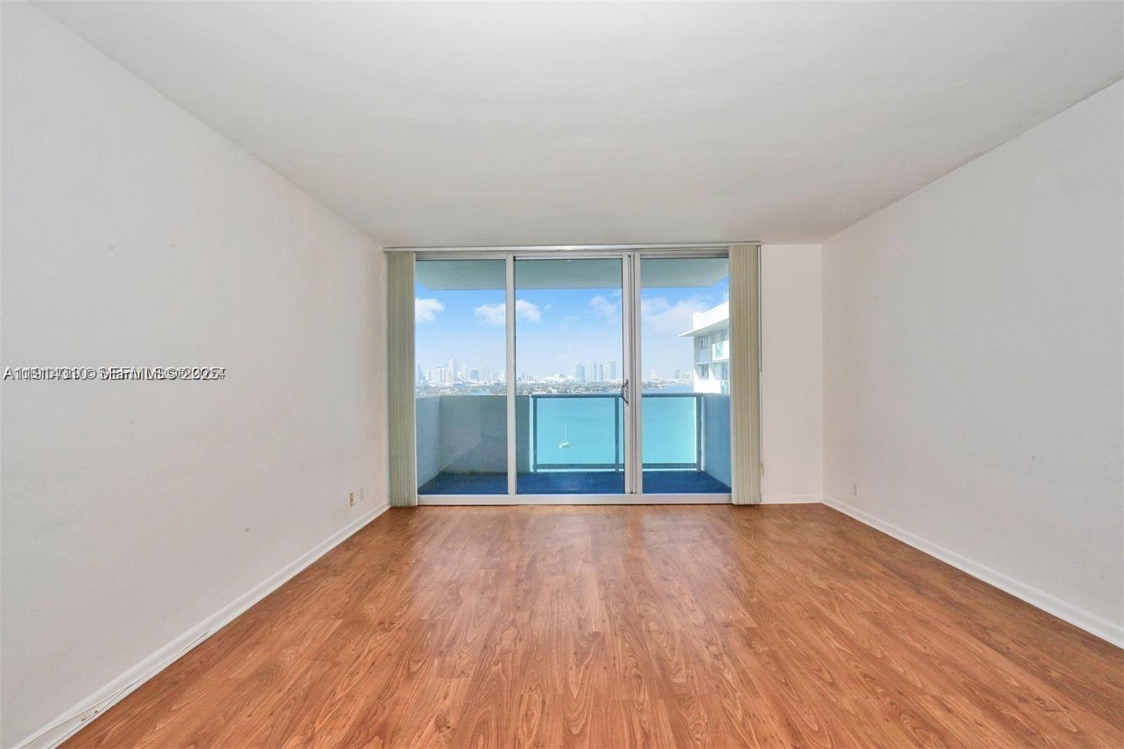 An empty room features wood-look flooring, white walls, and a sliding glass door overlooking water — 1200 West Ave # 1503, Miami Beach FL 33139, MIAMI BEACH, FL