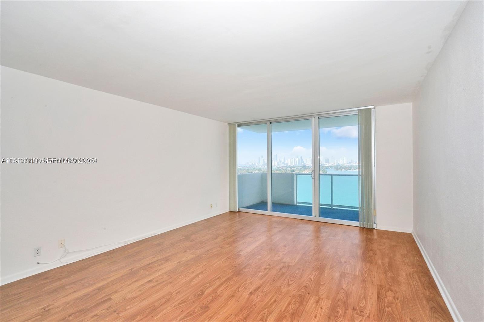 An empty room features wood-look flooring, white walls, and a sliding glass door with balcony access — 1200 West Ave # 1503, Miami Beach FL 33139, MIAMI BEACH, FL