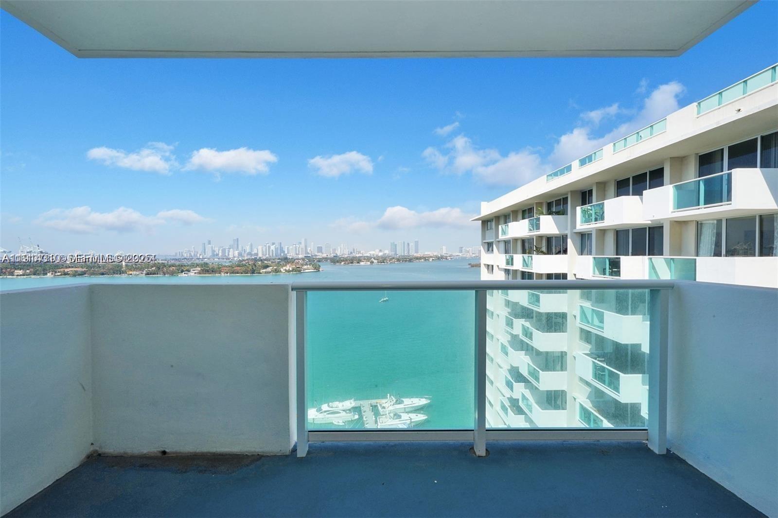 A balcony overlooks a bay with a distant city skyline and a neighboring apartment building — 1200 West Ave # 1503, Miami Beach FL 33139, MIAMI BEACH, FL