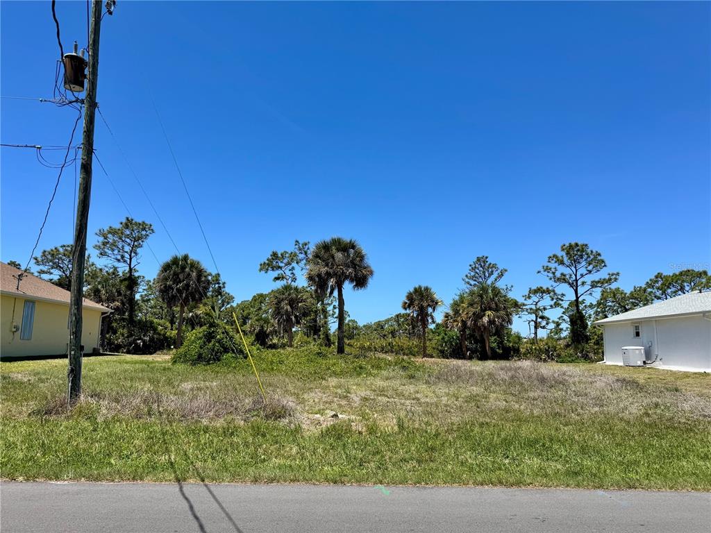 A vacant, grassy residential lot sits between two houses under a clear blue sky — 135 LONG MEADOW LANE, ROTONDA WEST, FL