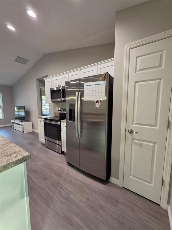 An open-concept living area features light gray walls, wood-look flooring, and a kitchen with white cabinets — 4244 SE 138TH STREET, SUMMERFIELD, FL