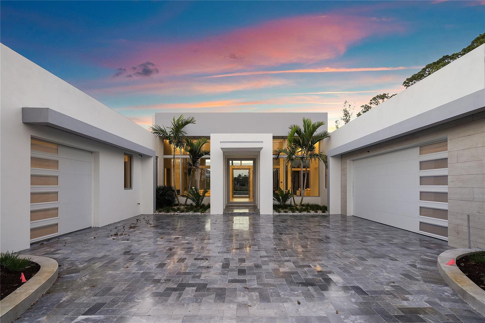 A modern house exterior features a stone-paved courtyard, two garages, and a central glass entrance — 5747 NW 63rd Way, Parkland FL 33067, PARKLAND, FL