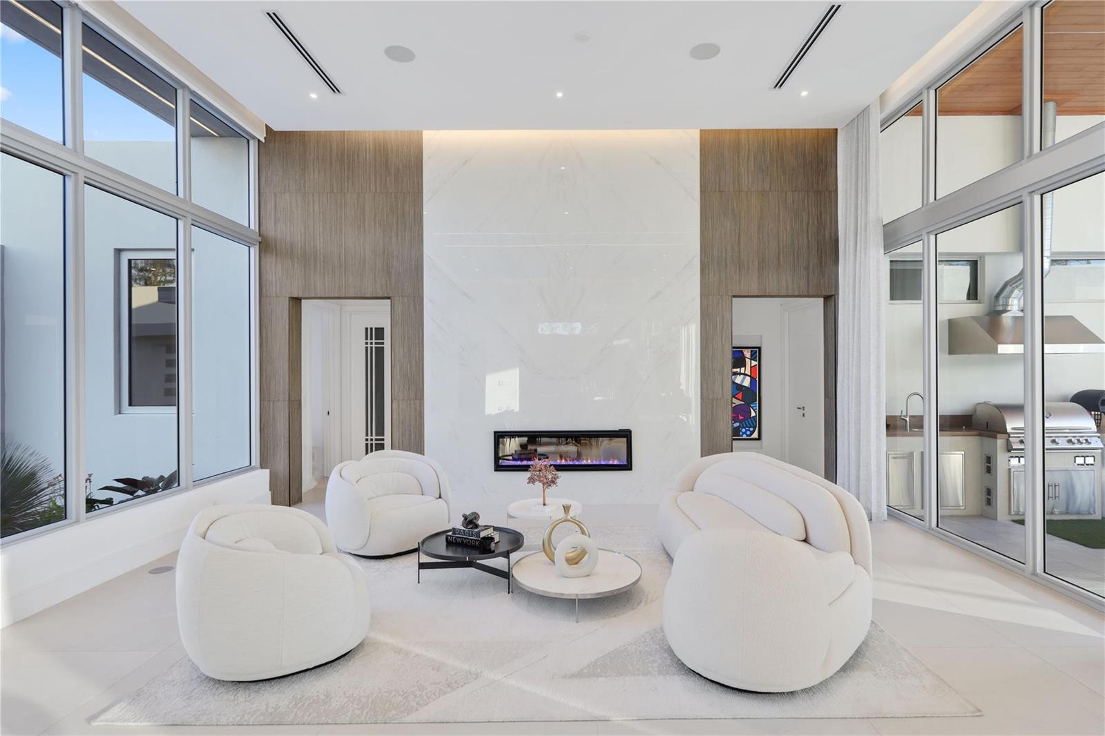A modern living room features a marble fireplace wall, white curved furniture, and floor-to-ceiling windows — 5747 NW 63rd Way, Parkland FL 33067, PARKLAND, FL
