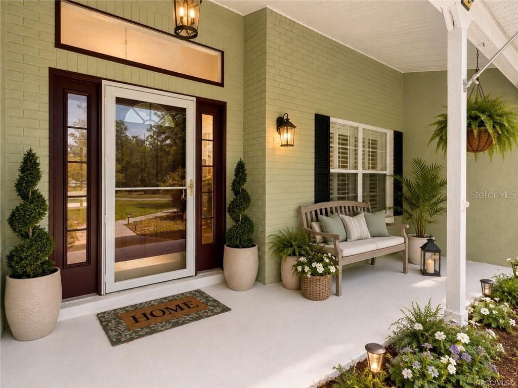 A covered front porch features a green brick exterior, a wooden bench, and potted topiary trees — 1852 W IVORYWOOD DRIVE, BEVERLY HILLS, FL
