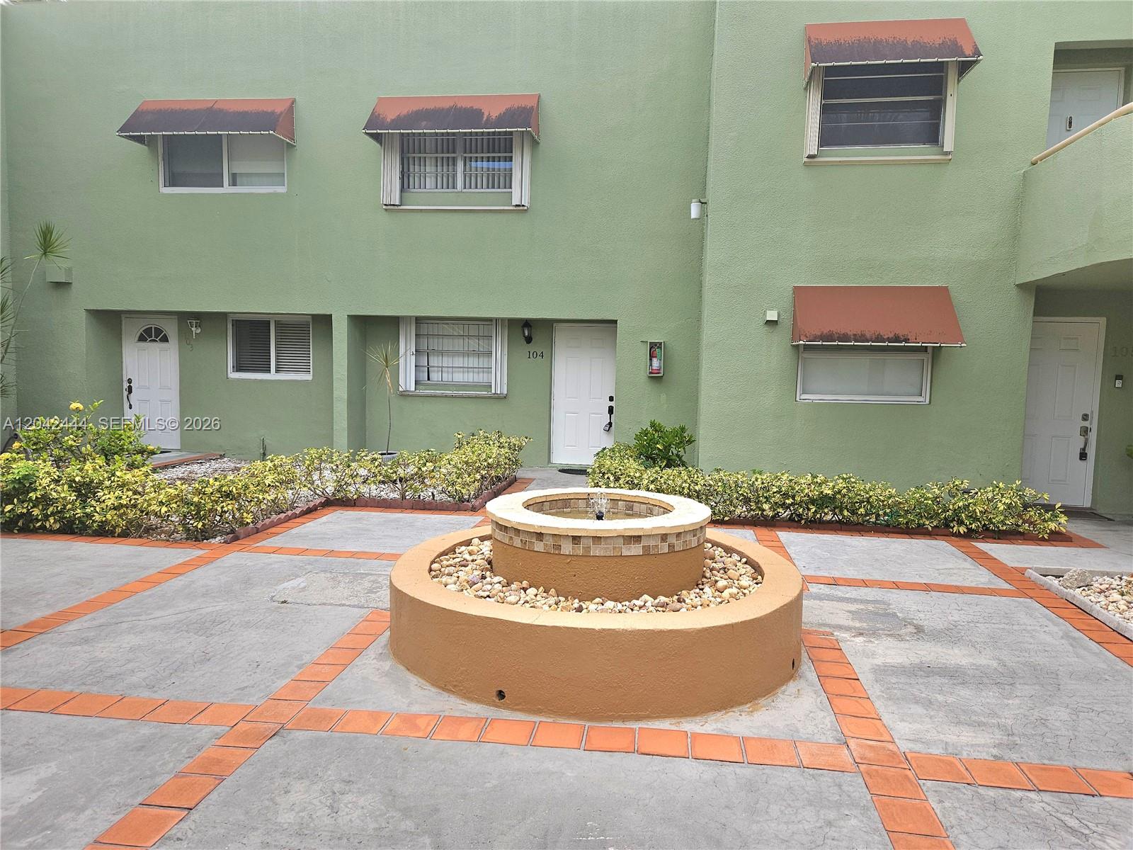 A green multi-unit building exterior features a central circular fountain and paved courtyard — 11071 NW 7th St # 15, Miami FL 33172, MIAMI, FL