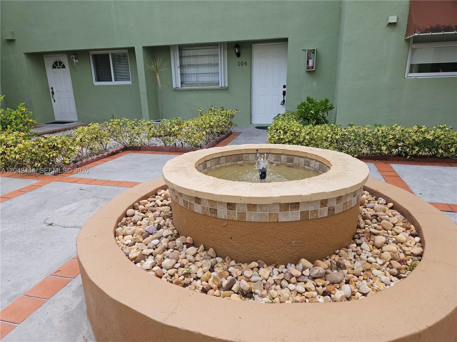 A round stone fountain sits in a courtyard in front of a green apartment building — 11071 NW 7th St # 15, Miami FL 33172, MIAMI, FL