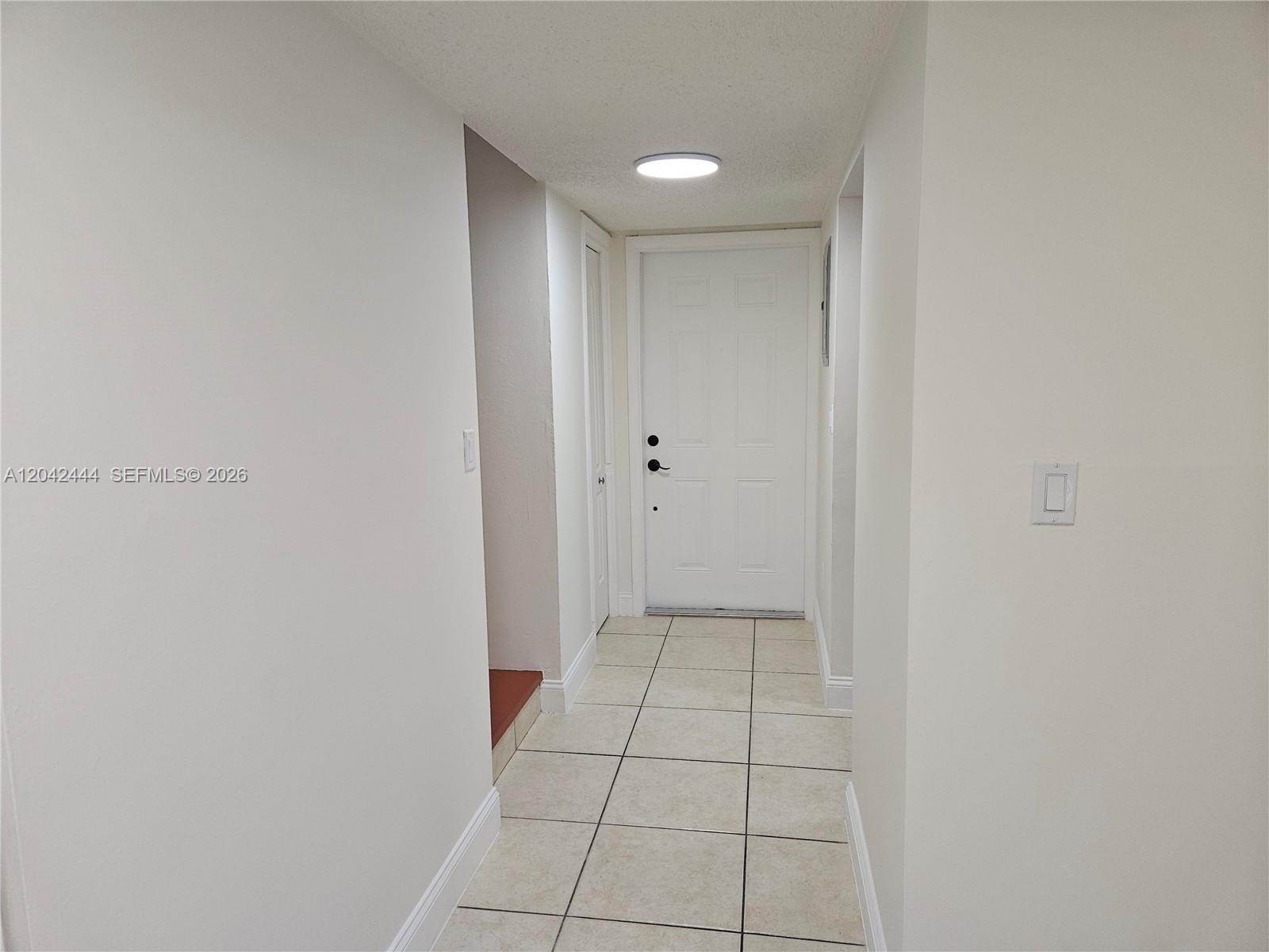 A white hallway features tiled flooring, a flush-mount ceiling light, and a white entry door — 11071 NW 7th St # 15, Miami FL 33172, MIAMI, FL