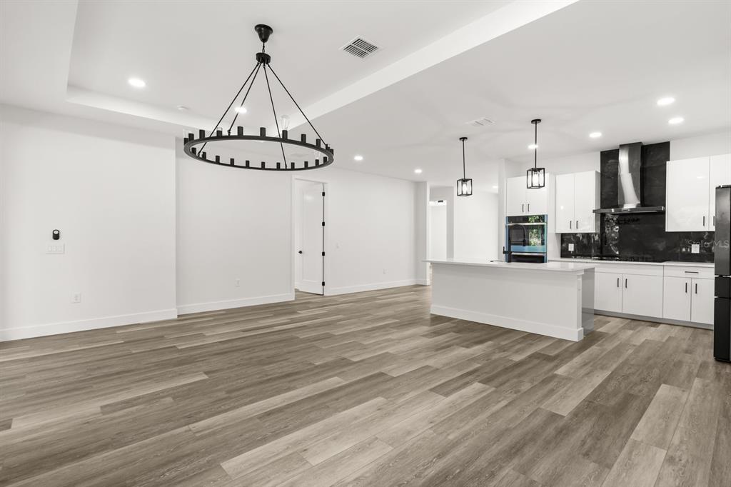 A modern open-concept kitchen and dining area featuring white cabinetry, a large island, and wood-look flooring — 321 WATER SHORE DRIVE, LEESBURG, FL