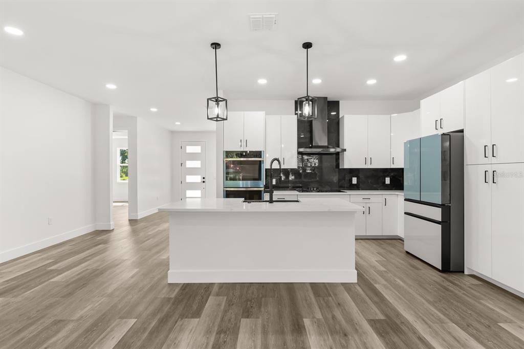 A modern kitchen features white cabinets, a central island, stainless steel appliances, and wood flooring — 321 WATER SHORE DRIVE, LEESBURG, FL