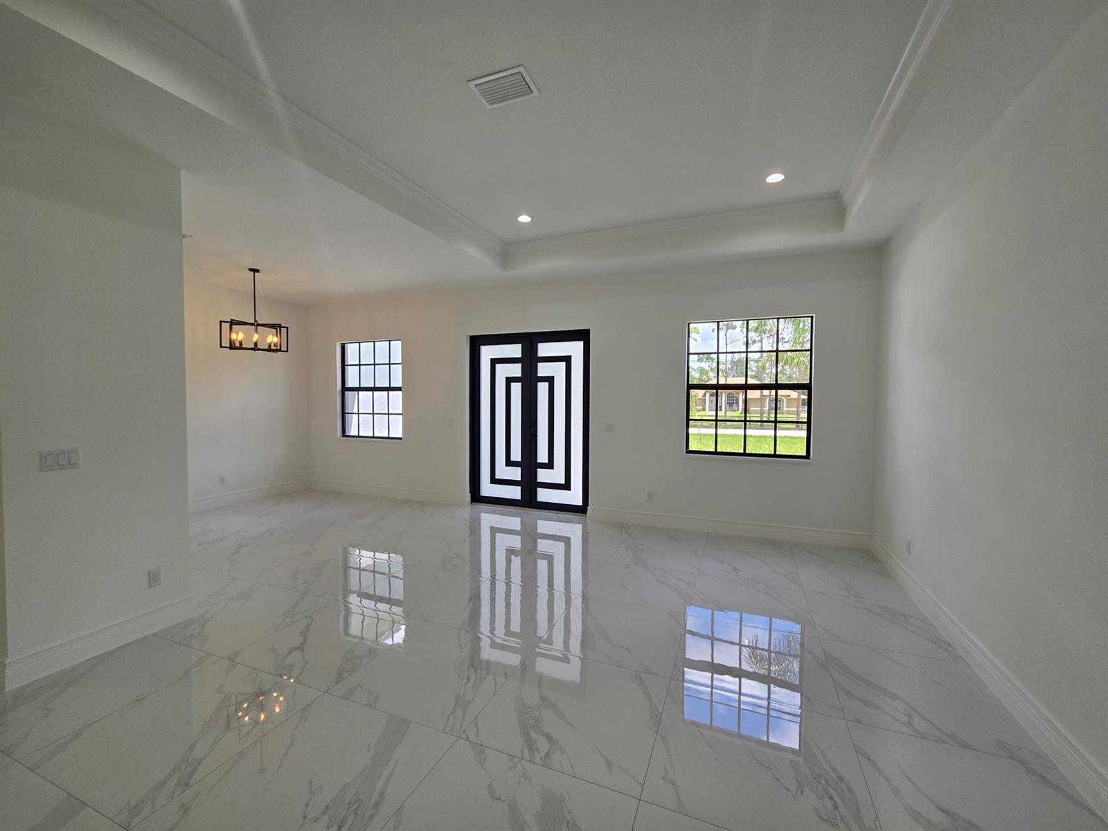 A bright, empty room features white marble-look tile floors, a tray ceiling, and a modern door — 14974 N 77th Pl Place N, Loxahatchee FL 33470, LOXAHATCHEE, FL