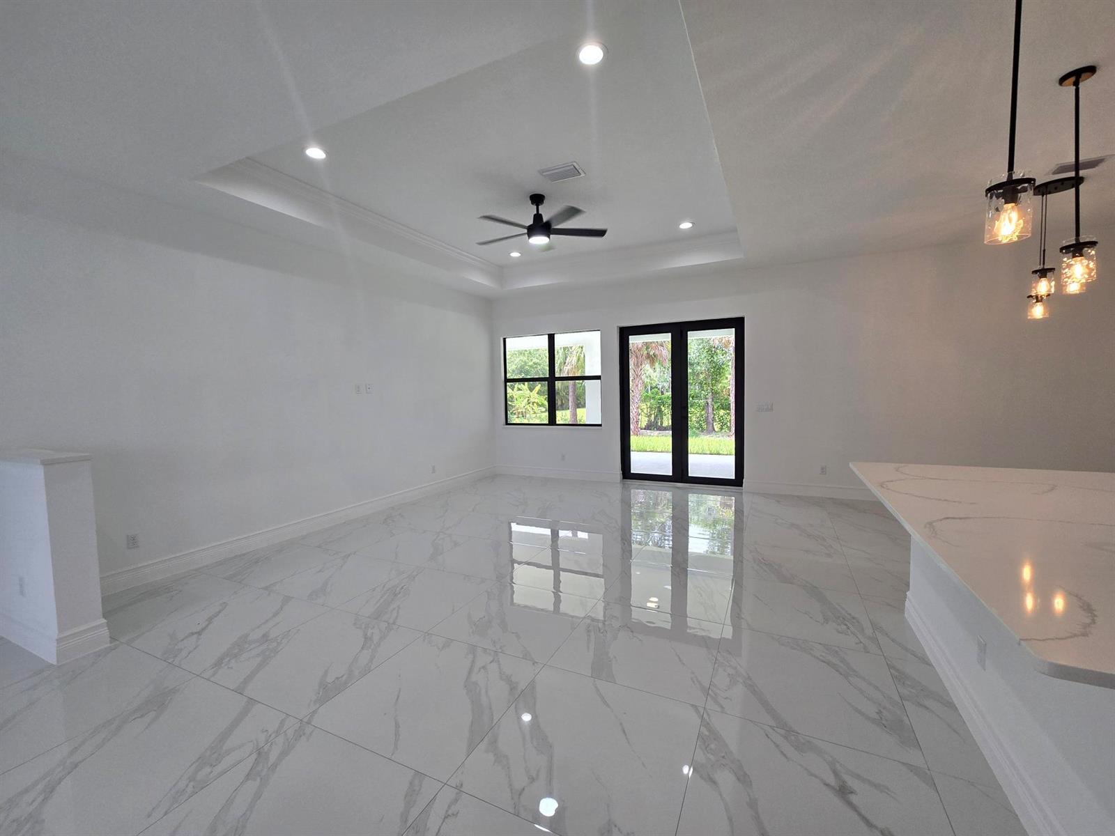 A bright living room features white marble-look tile floors, a tray ceiling, and glass doors — 14974 N 77th Pl Place N, Loxahatchee FL 33470, LOXAHATCHEE, FL
