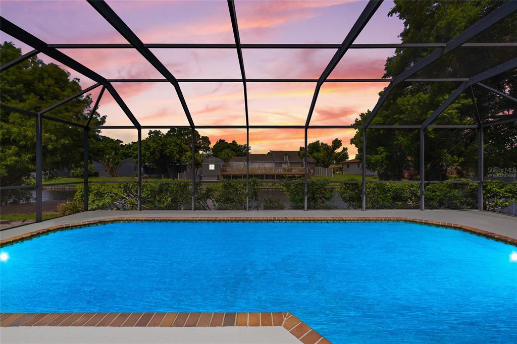 A screened-in patio features wicker furniture, a glass-top coffee table, and a view of a pool — 1116 76TH STREET NW, BRADENTON, FL