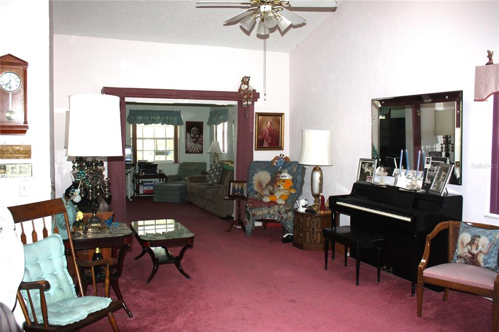 A living room with red carpeting, a black piano, and an arched doorway to another room — 18 BRISTOL DRIVE, PALM COAST, FL