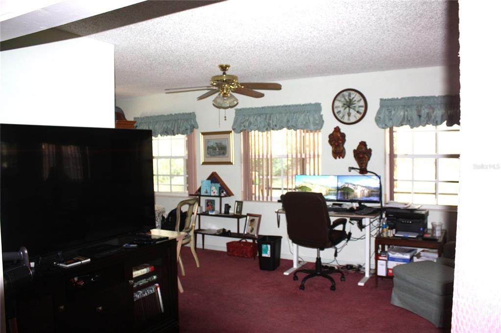 A living room with red carpeting, a large television, and a computer desk area — 18 BRISTOL DRIVE, PALM COAST, FL