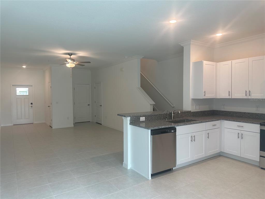 A kitchen with white cabinets and granite countertops overlooks an open-concept living area with tile floors — 17664 NECTAR FLUME DRIVE, LAND O LAKES, FL