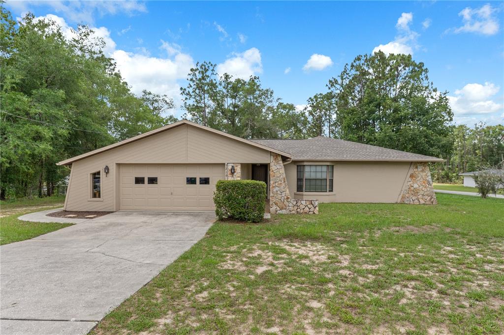 A single-story house with a beige exterior, stone accents, a two-car garage, and a lawn — 5216 E HOPP LANE, INVERNESS, FL