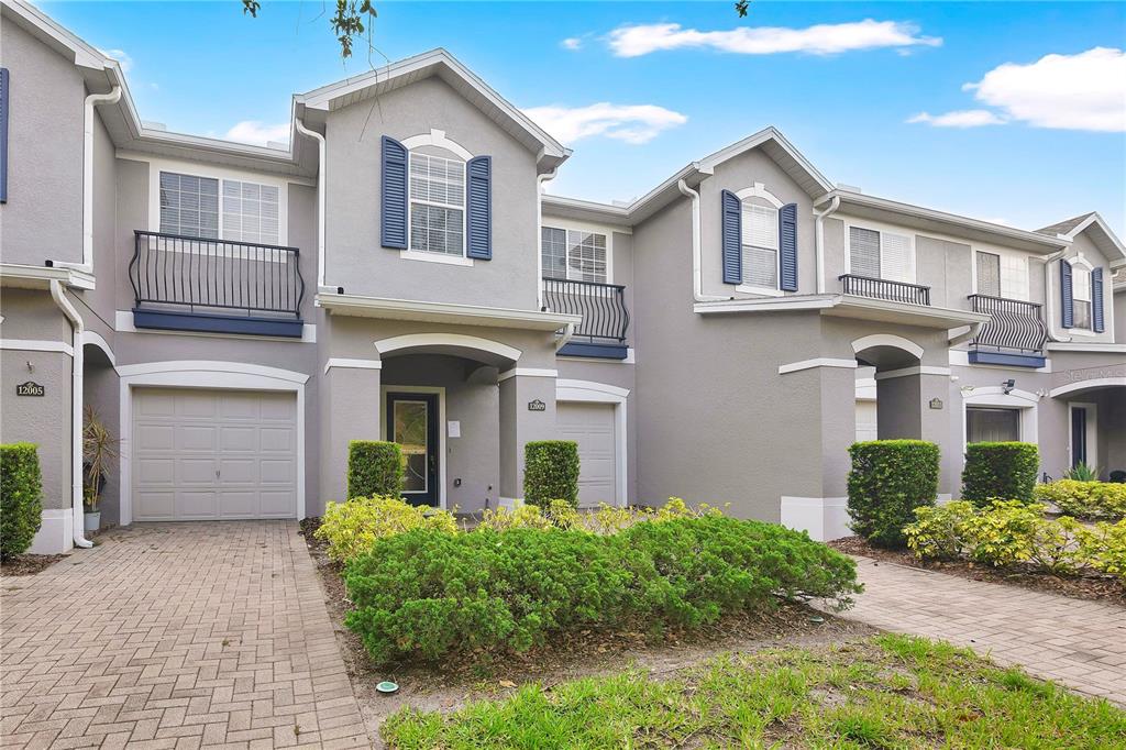 A row of two-story townhomes with gray stucco exteriors, paved driveways, and small balconies — 12009 GREAT COMMISSION WAY, ORLANDO, FL