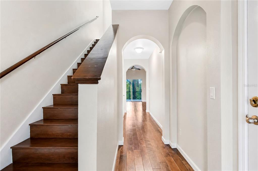 A staircase with wood treads sits beside a hallway featuring arched openings and wood flooring — 12009 GREAT COMMISSION WAY, ORLANDO, FL