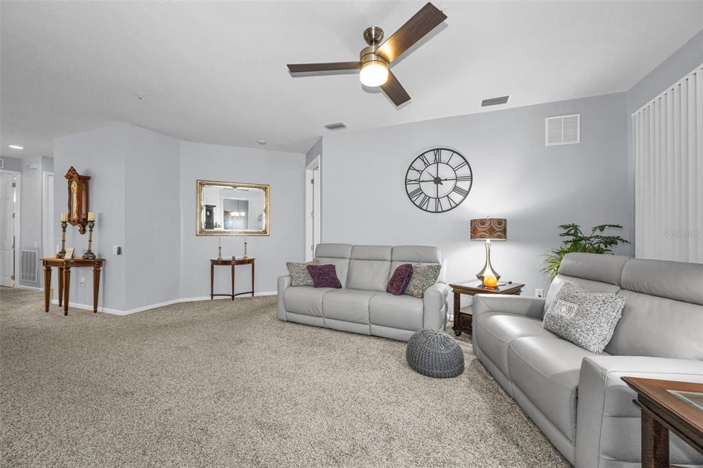 A living room features light gray walls, carpeted flooring, two leather sofas, and a ceiling fan — 889 LANTERN WAY, CLEARWATER, FL