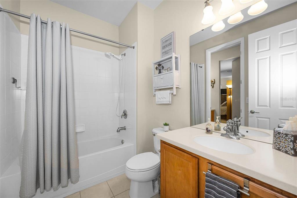 A bathroom features a tub-shower combination, a wood vanity with a sink, and a toilet — 889 LANTERN WAY, CLEARWATER, FL