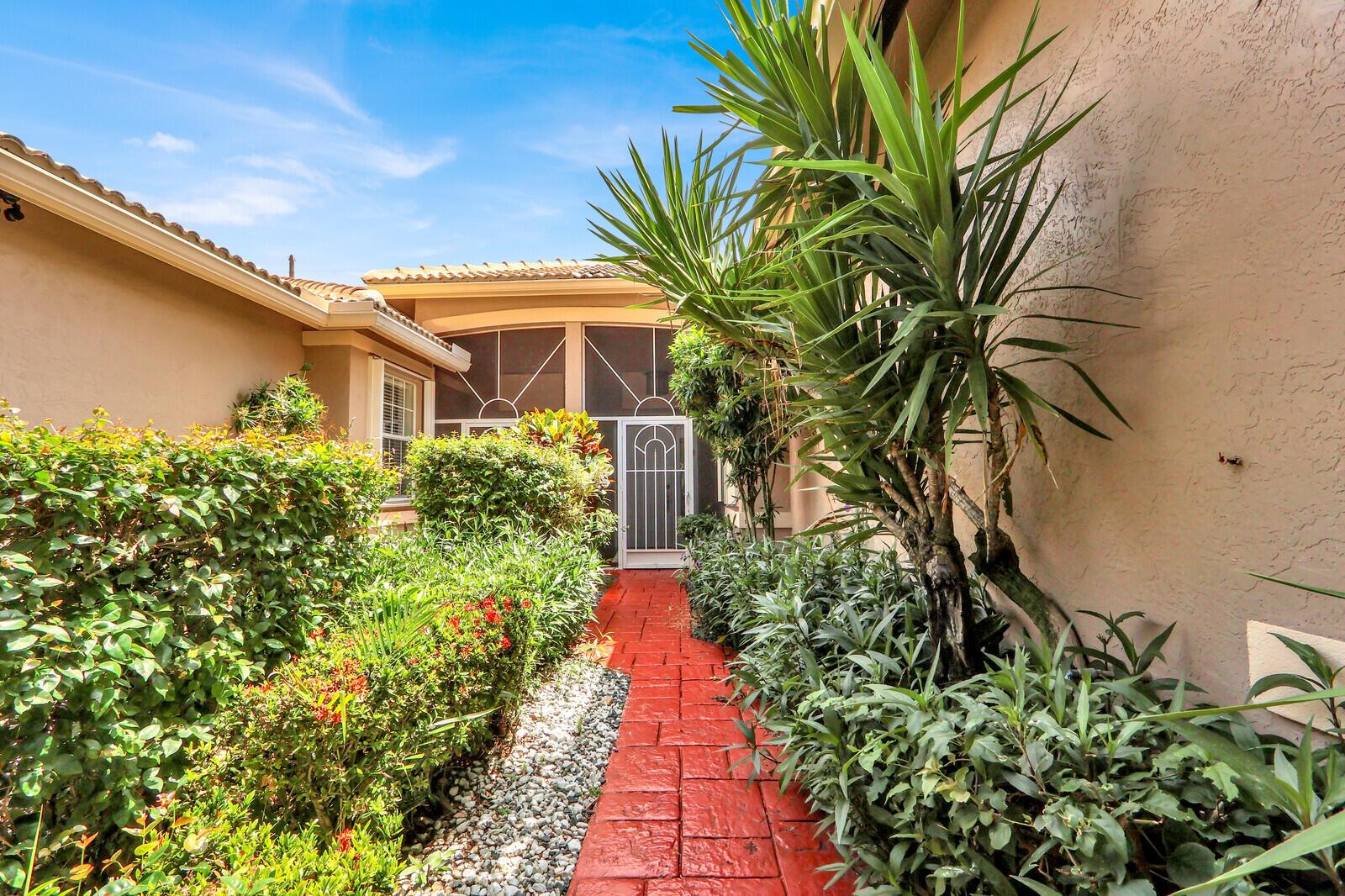 A red brick walkway leads to a screened front entryway surrounded by lush green landscaping — 9531 Crescent View Drive N, Boynton Beach FL 33437, BOYNTON BEACH, FL