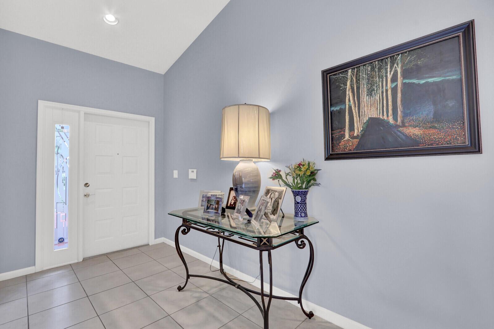 An entryway features light blue walls, a glass-topped console table, and a framed landscape painting — 9531 Crescent View Drive N, Boynton Beach FL 33437, BOYNTON BEACH, FL