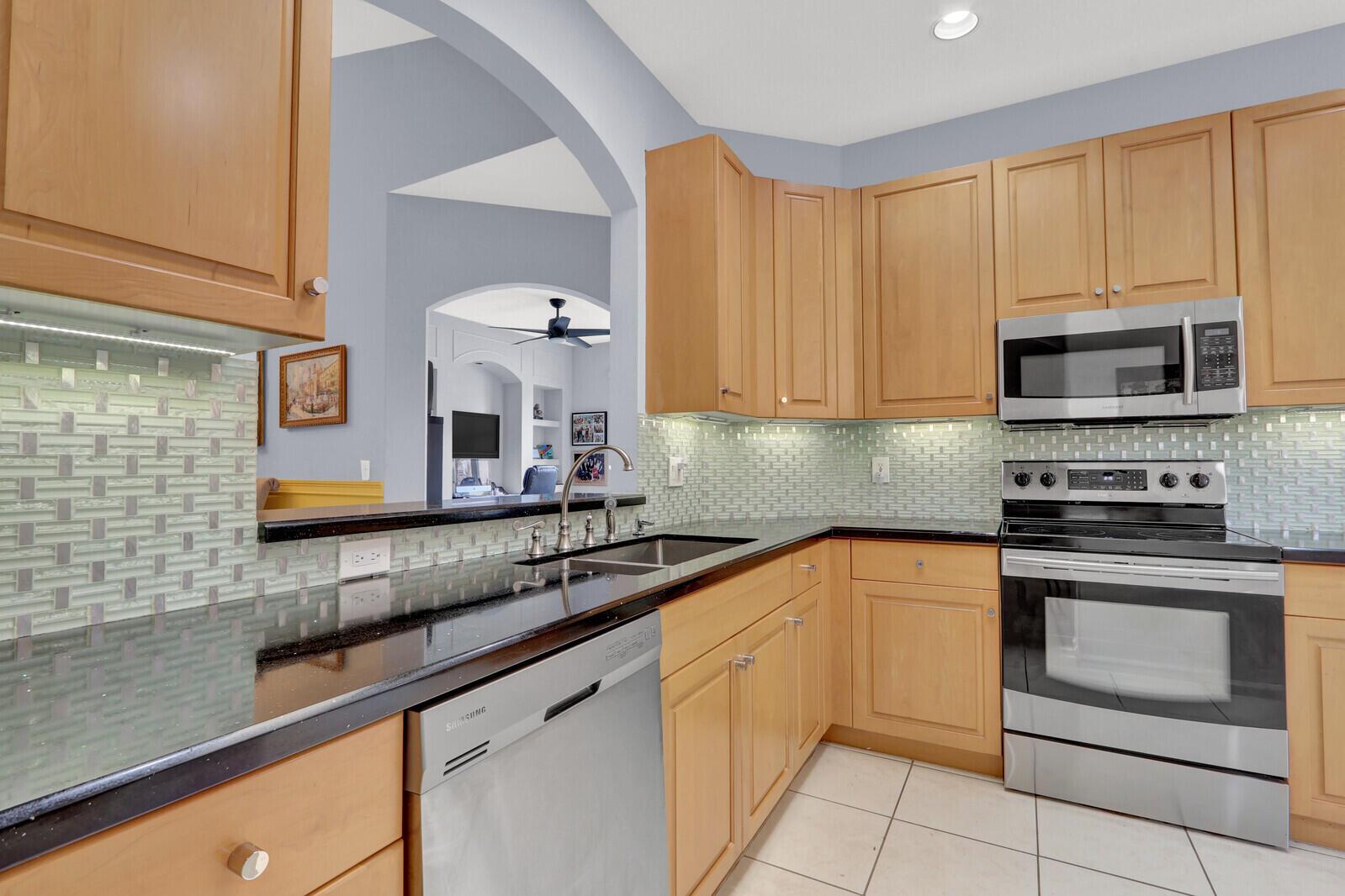 A kitchen with light wood cabinets, black countertops, stainless steel appliances, and a glass tile backsplash — 9531 Crescent View Drive N, Boynton Beach FL 33437, BOYNTON BEACH, FL
