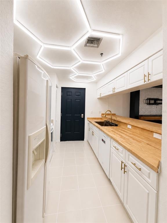 A kitchen features white cabinets, wood countertops, tile flooring, and a geometric LED ceiling light — 2002 E 5TH AVENUE UNIT 112, TAMPA, FL