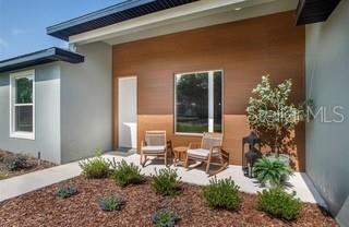 A modern home entrance features a wood-paneled wall, two rocking chairs, and landscaped mulch — 630 MARION OAKS BLV, OCALA, FL