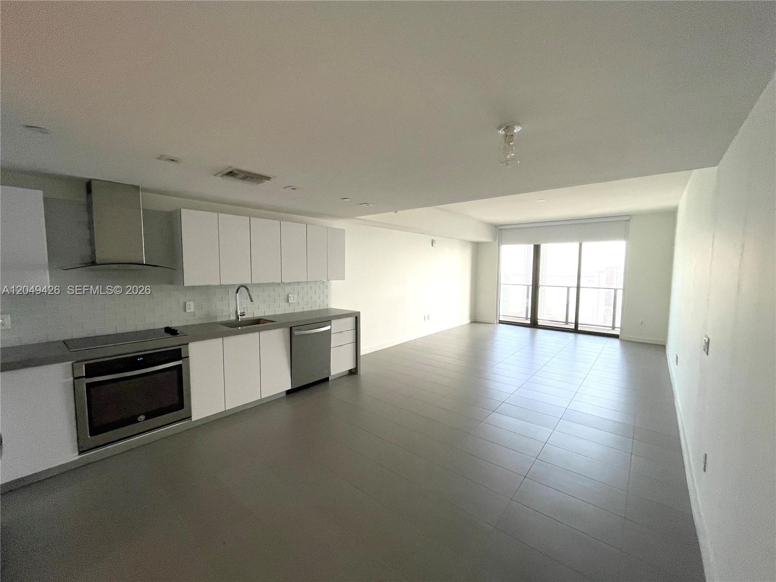 A modern kitchen with white cabinets and stainless steel appliances opens into a tiled living area — 1600 NE 1st Ave # 3603, Miami FL 33132, MIAMI, FL