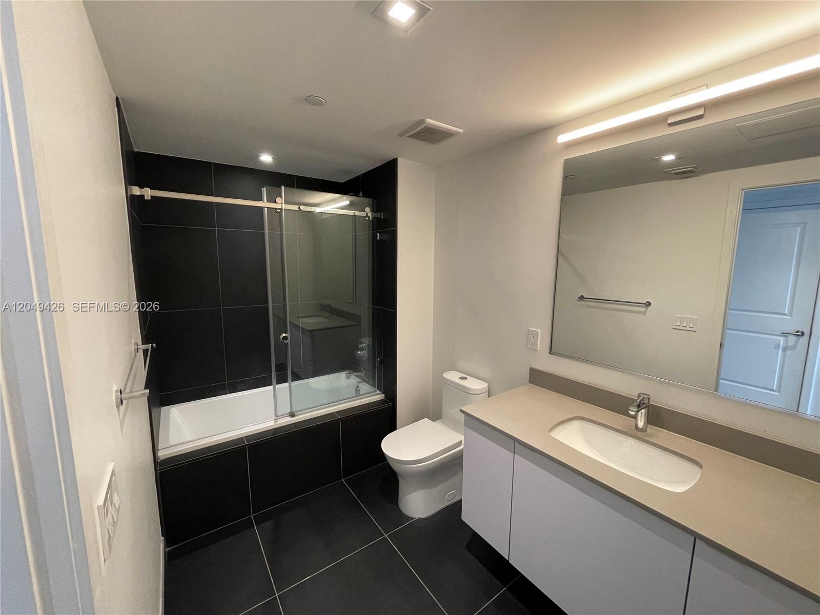 A modern bathroom features a black-tiled bathtub enclosure, a white vanity, and a large mirror — 1600 NE 1st Ave # 3603, Miami FL 33132, MIAMI, FL